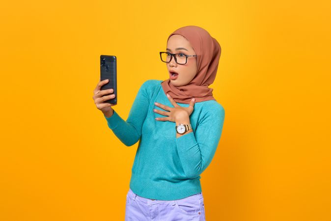 Surprised Muslim woman taking video call on her phone