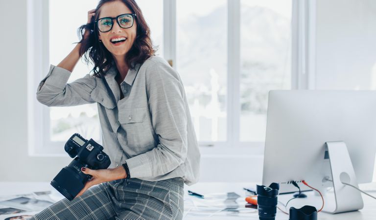Woman with dslr camera in white office and smiling