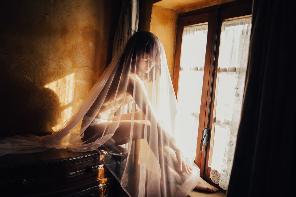 Sensual woman under veil near window