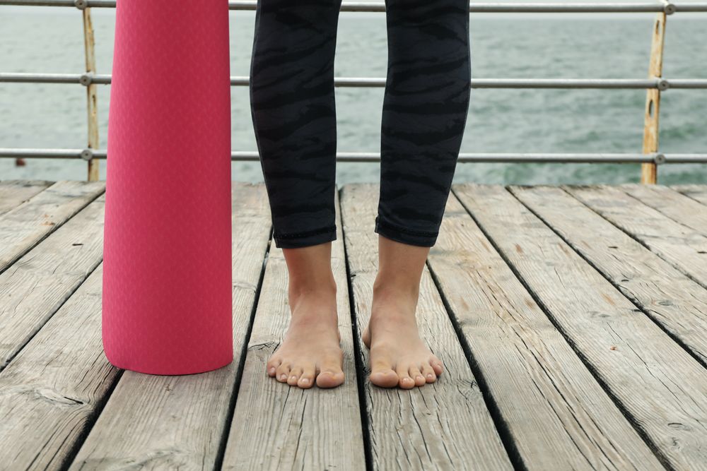 Female legs and pink yoga mat on wooden floor outdoors