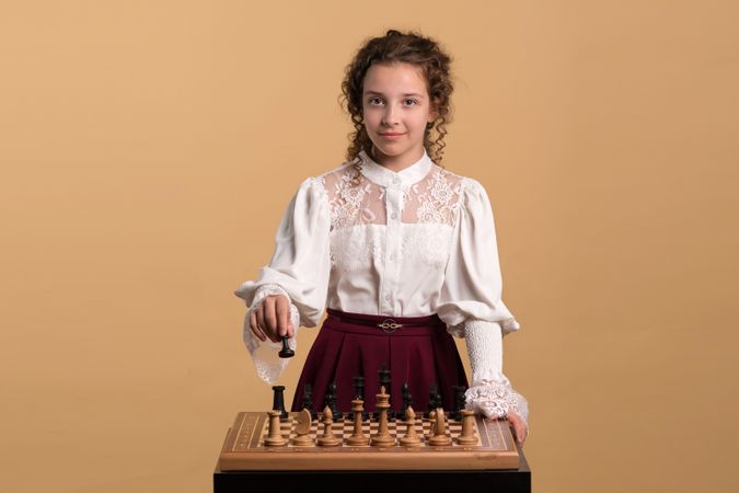 Young girl in vintage lace blouse playing chess thoughtfully.