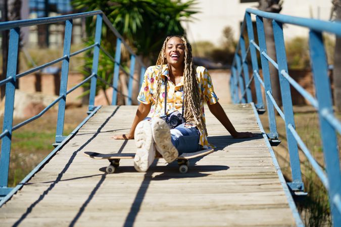 Female sitting on pedestrian bridge with skateboard on sunny day