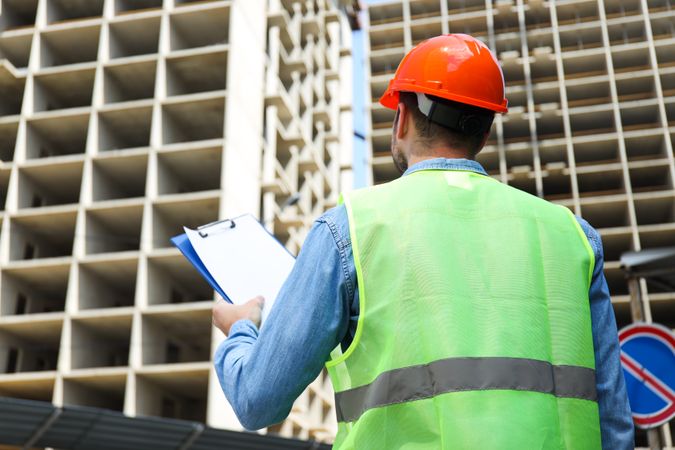 Civil engineer in safety hat with clipboard against construction