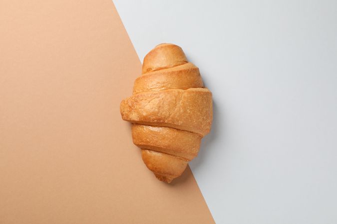 Freshly baked croissant on nude two tone background, top view