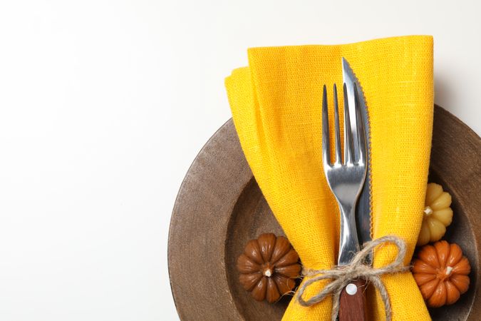 Cutlery with yellow napkin on wooden plate on light background, close up