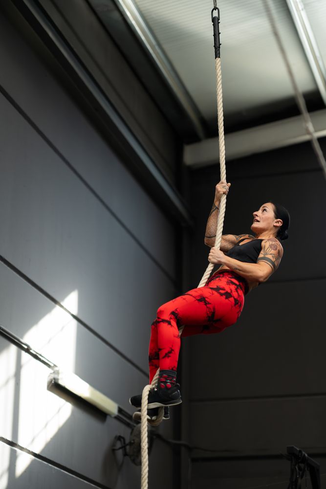 Strong fit woman climbing rope in gym