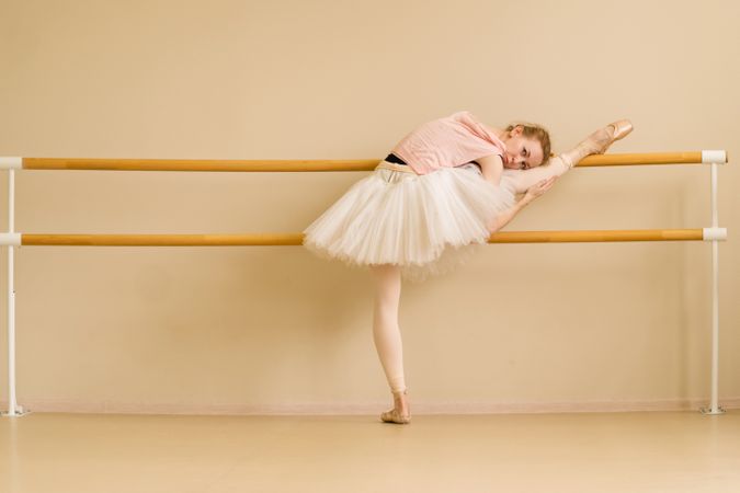 Ballet dancer rests on barre, holding stretch with leg raised