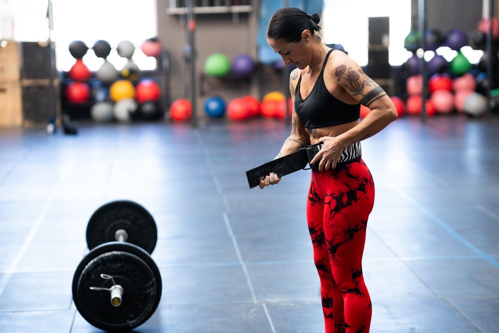 Woman adjusting weight lifting belt next to bar bell