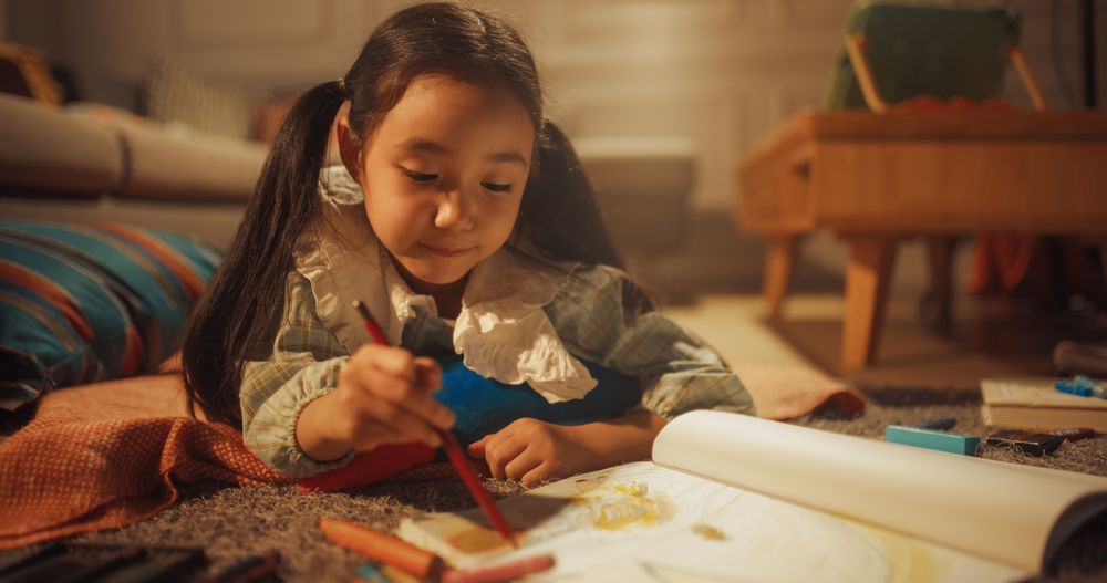 Portrait of Cute Little Girl Drawing while Lying on the Floor in Living Room.