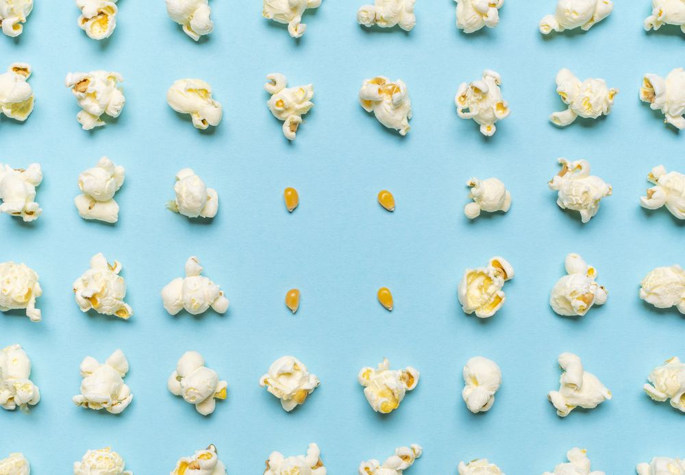 Popcorn flakes and corn kernels aligned on a blue background