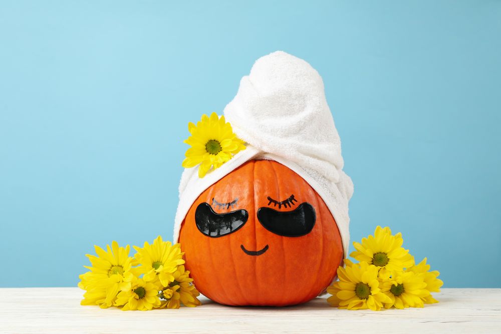 Pumpkin with towel, flowers and under eye patches against blue background