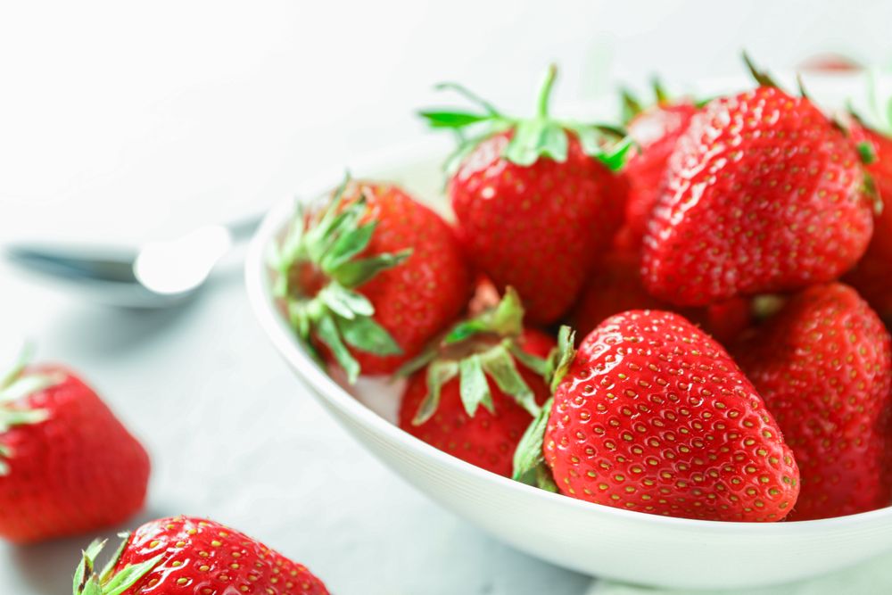 Plate with fresh strawberries and spoon on bright wooden background, closeup and space for text