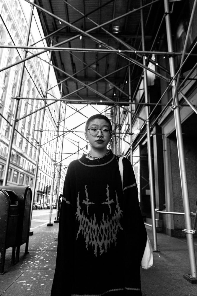 Grayscale photo of woman in long dress standing under scaffolding on sidewalk