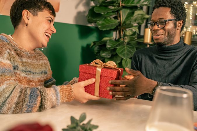 Happy diverse couple laughing while exchanging a gift at a party