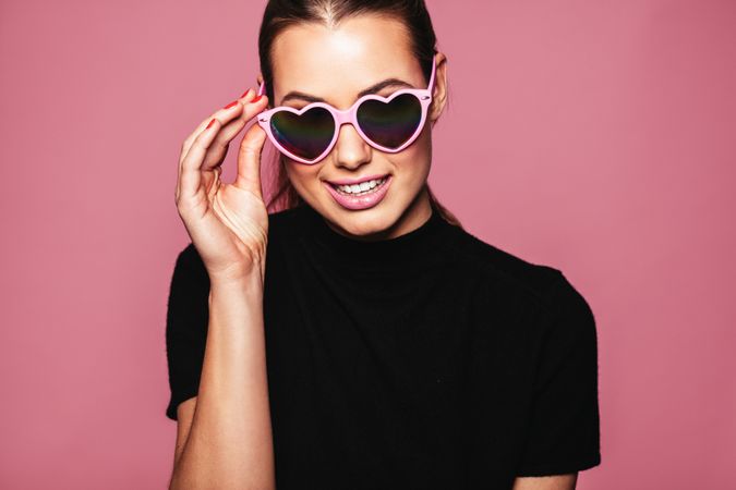 White woman posing with glasses against pink background