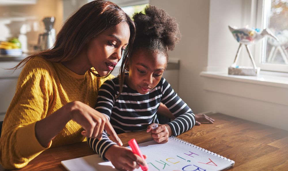 Black mother and daughter writing the alphabet at home