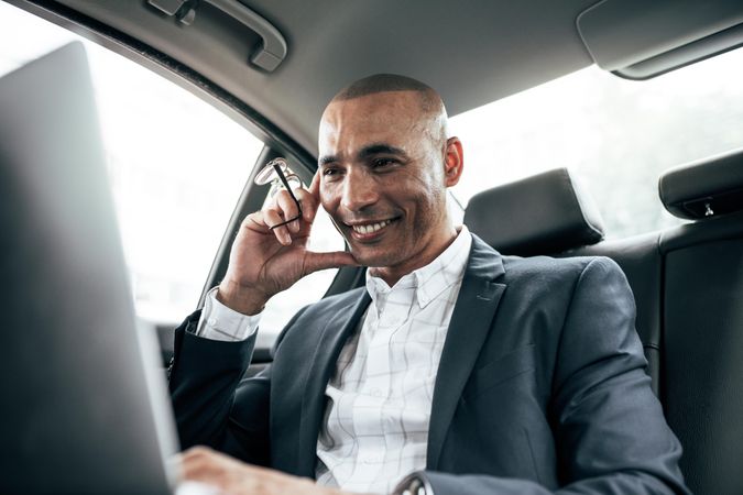 Smiling man holding eyeglasses in hand doing work while sitting in car