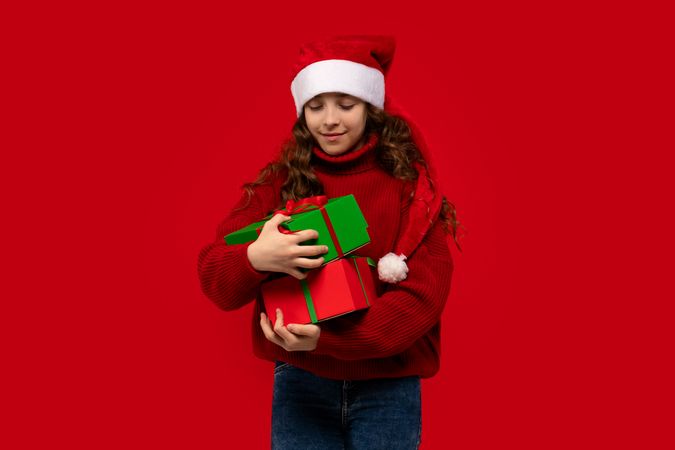 Girl in Santa hat carefully balances Christmas presents.