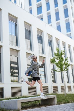Woman with tablet in stylish suit jumping holding sunglasses