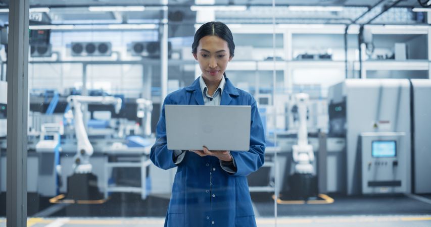 Electronics Manufacture Engineer Smiling and Working. Young Asian Female Using Laptop Computer for Online Research, Monitoring Industrial Artificial Intelligence Systems