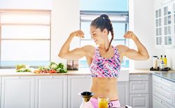 Woman flexing her arms in bright kitchen with vegetables on the counter