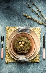 Top view of decorative eggs in delicate nest on ceramic pink plate on placemat with pussy willow with copy space