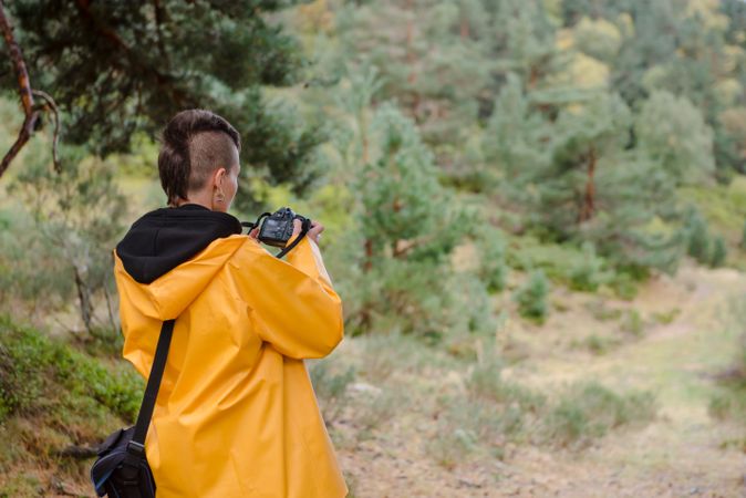 Enthusiastic person in yellow raincoat photographing tree in mountain
