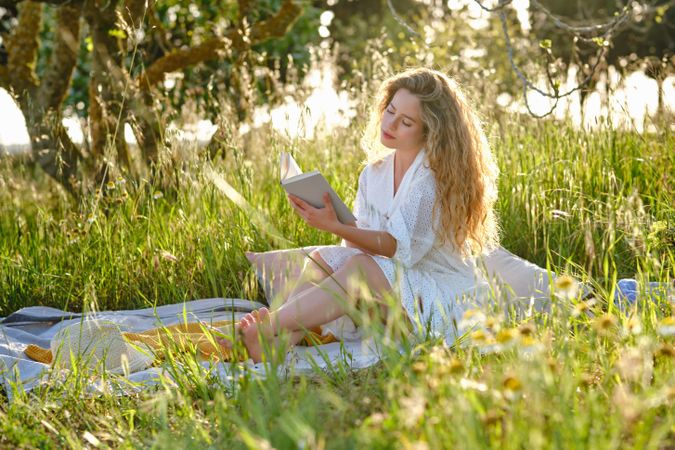 Woman reading book on grassy verdant glade