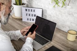 Back view of middle aged man holding a smartphone sitting on his home desk 0VJ9j0