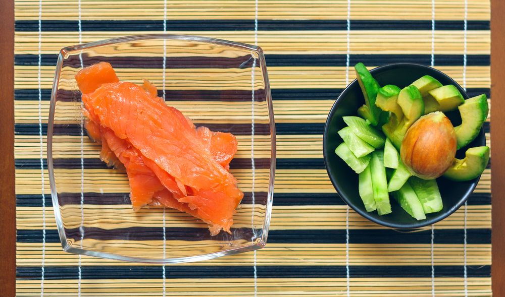 Top view of bowls with avocado, cucumber and salmon cut ready to prepare sushi