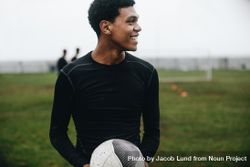 Smiling soccer player standing on field holding a football looking away 41aRg4