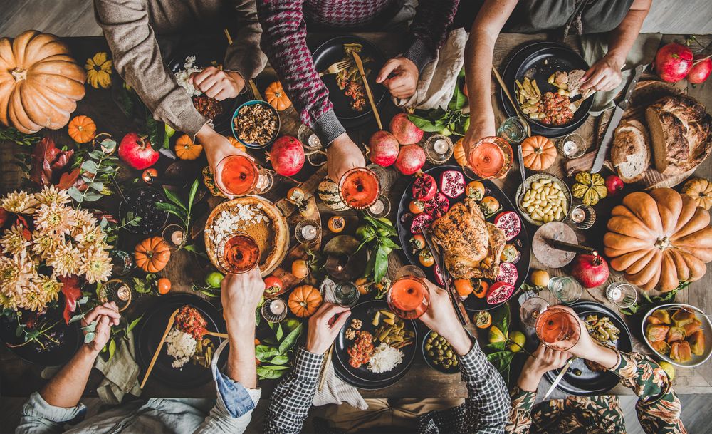 Group of people toasting with wine at festive table setting with roast chicken, squash, and pie