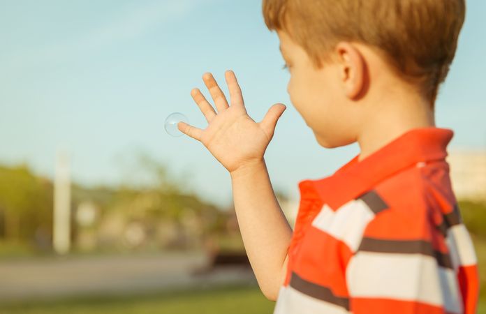 Cute boy looking soap bubble in his open hand