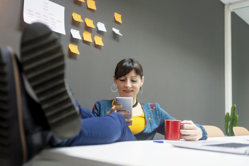 Smiling businesswoman with mug using smartphone