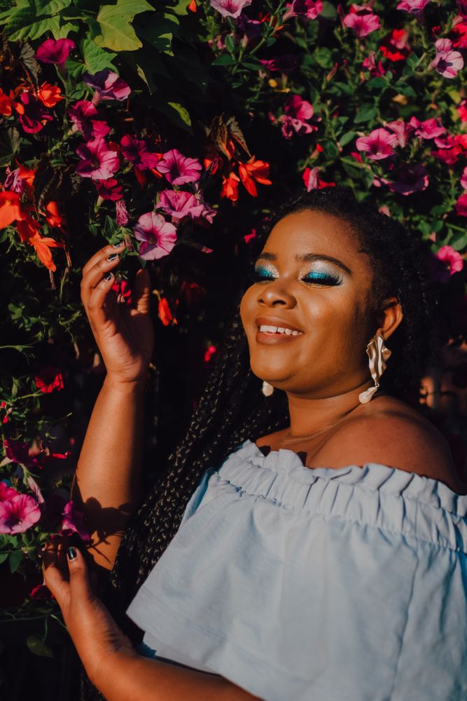 Joyful trendy Black woman standing beside blossomed tree