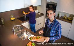 Couple looking up at camera while cutting vegetables in the kitchen preparing food 4dZXL0