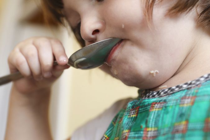 A small kid learning how to eat soup on her own.