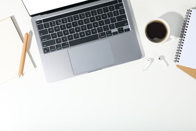 Top view of table with open laptop, earbuds, coffee, and blank notebooks with copy space