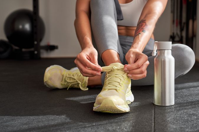 Crop sportswoman tying shoelaces in gym