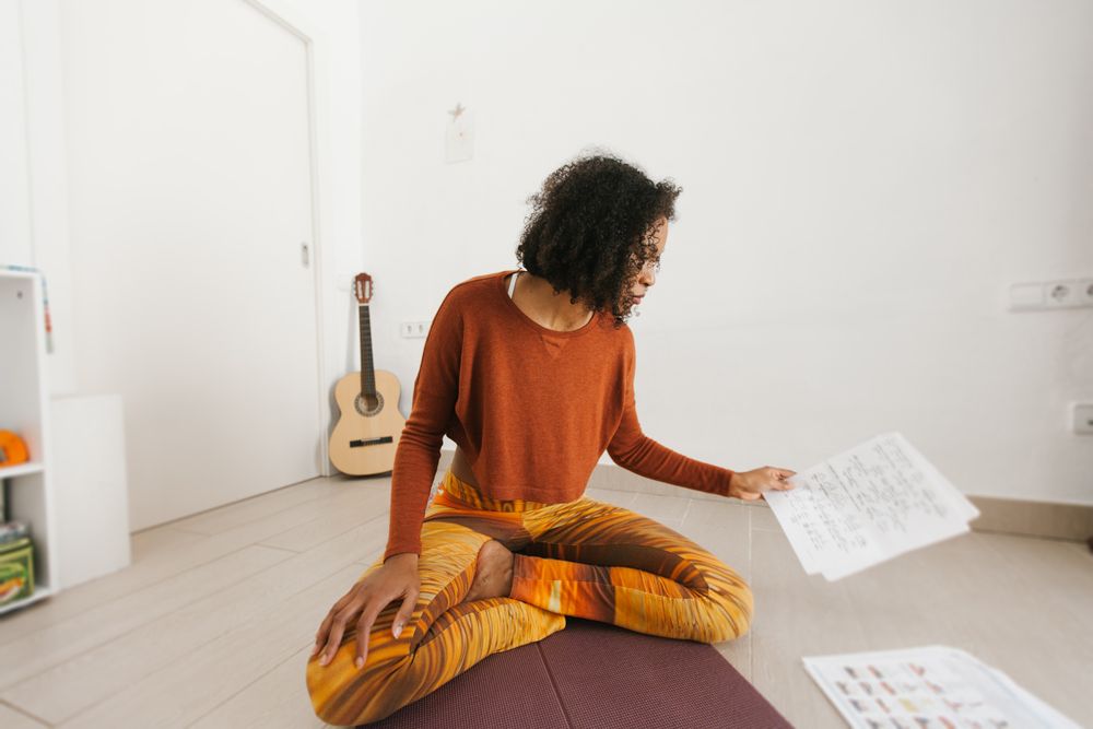 Sportive woman sitting with legs crossed on floor studying routine paper