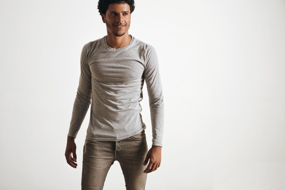 Smiling man in grey shirt and jeans on a blank background