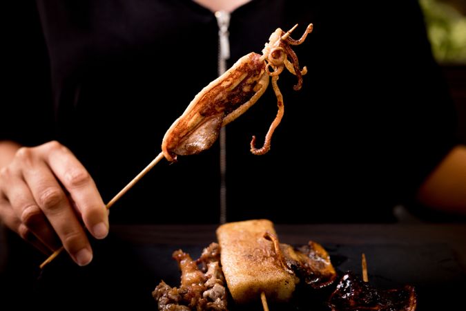Woman eating grilled squid skewer in restaurant