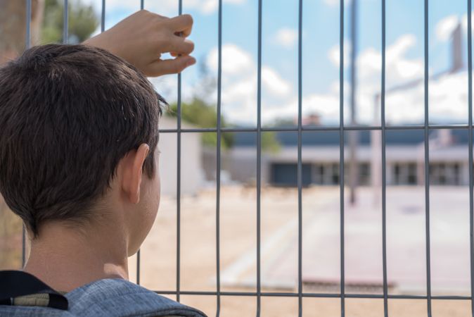 Back of boy holding gate looking into school yard
