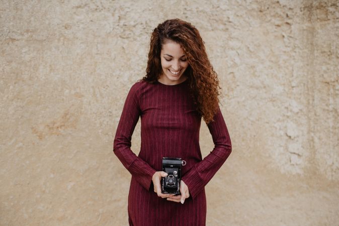 Cheerful woman with camera near rough wall