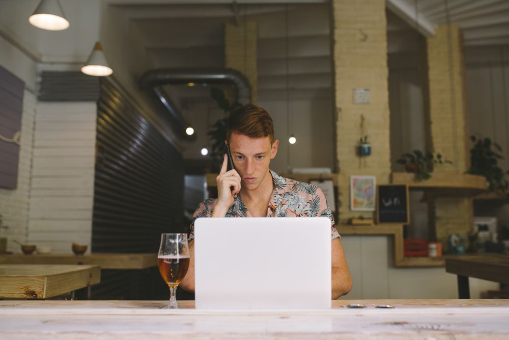 Man talking on smartphone while browsing laptop