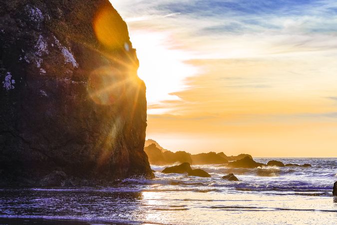 Sun half behind an ocean cliff with sunflare