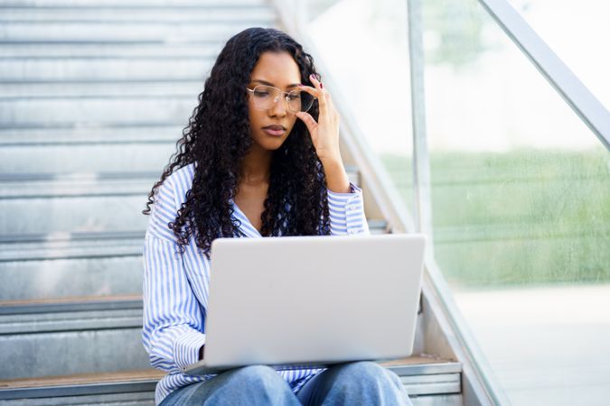A Focused Young Woman is Deeply Engaged in Her Work on a Laptop While Sitting on Stairs