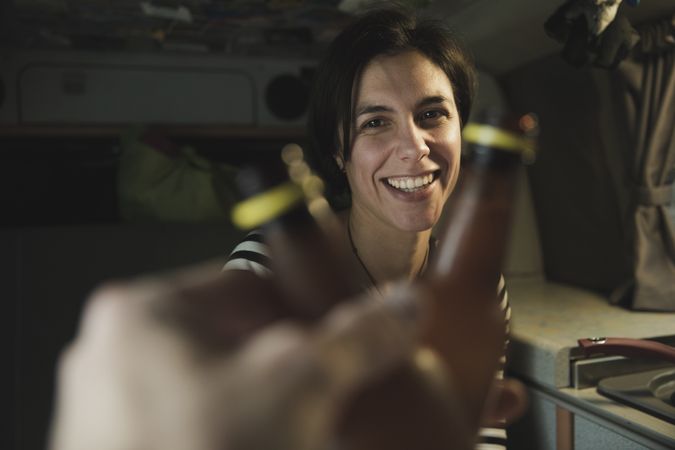 Smiling woman clanging bottles with person near cooker in camper van