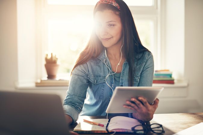 Content woman working on laptop in home office with earbuds and tablet