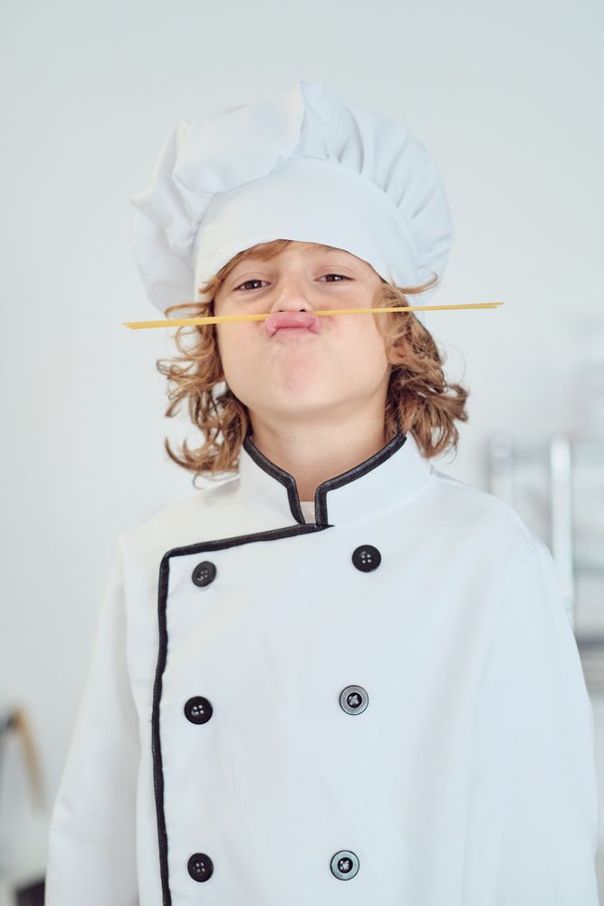 Amusing boy in chef uniform imitating mustache with spaghetti st